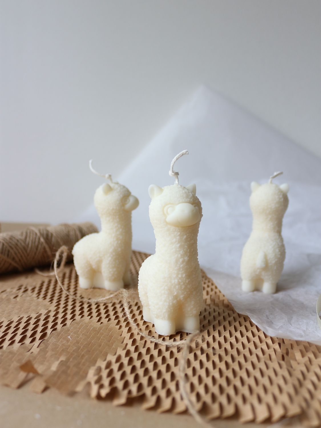tre candele a forma di alpaca in cera naturale bianca, disposte su tre lati diversi: frontale, laterale e posteriore