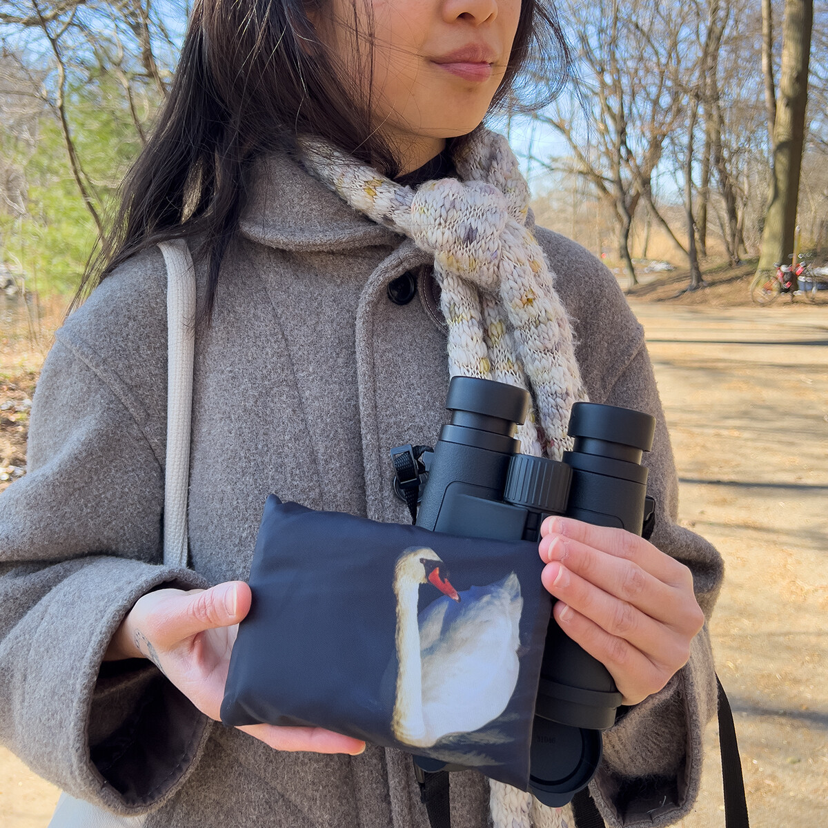 Person holding collapsible Swan shopping bag in a park, wildlife-inspired reusable tote by Dennis Newsham