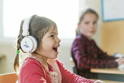 A girl wearing ear defenders to protect her ears. smiles in her classroom.
