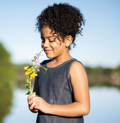 A girl smells some flowers she is holding in her hands outdoors.