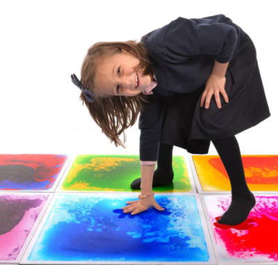 A girl bends down to touch the liquid floor tile she is playing on.