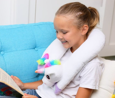A girl is wearing a vibrating neck cushion unicorn toy and smiling. 