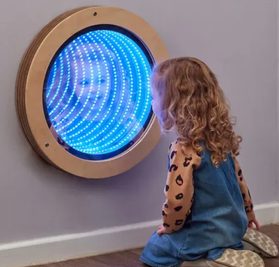 A girl kneels in front of a wall mounted infinity mirror.