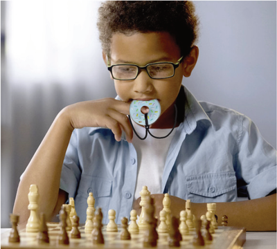 Boy playing chess while chewing on a sensory chew while concentrating.