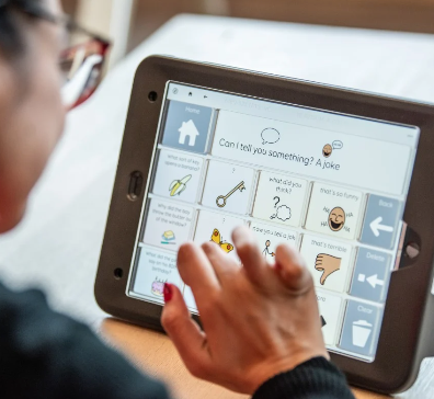 A lady types on a communication device using symbols. Grid 3 software with a keyguard for accuracy.