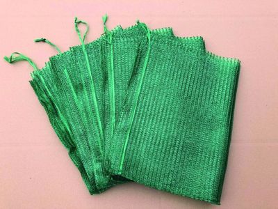 Five green net folded bags on a peach background