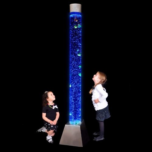 Two children looking at a tall bubble tube lit in blue