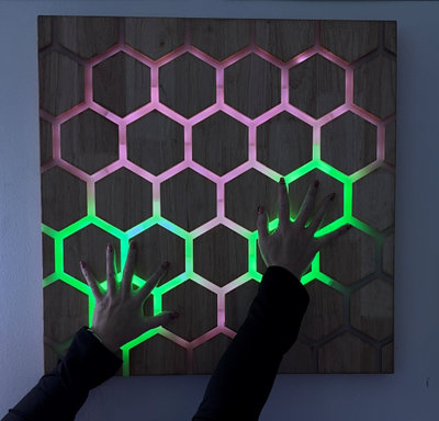 Touch interactive honeycomb panel in low light with hands activating colour change 