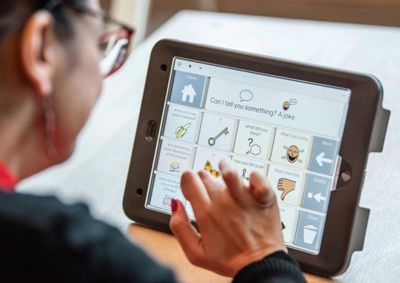 Girl typing on AAC software on a tablet using symbols.