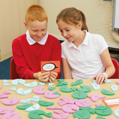 Two children sitting at a table interacting with foam equivalence circles 
