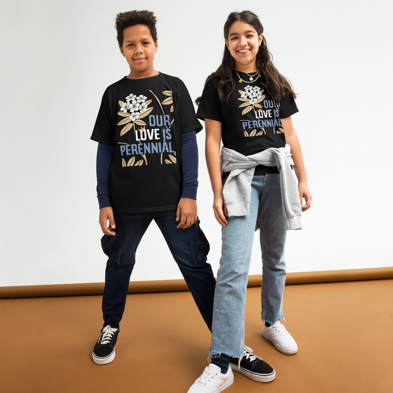 two children wearing black T-shirts with design of light blue and white lettering &quot;OUR LOVE IS PERENNIAL&quot; and rhododendrons with white blossoms and gold leaves
