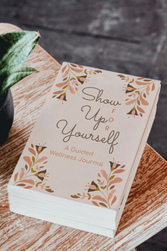 Show Up FOR Yourself Christian 21-day guided journal lying flat on a wooden coffee table next to a green potted plant, emphasizing mindfulness and holistic wellness for Christian women.