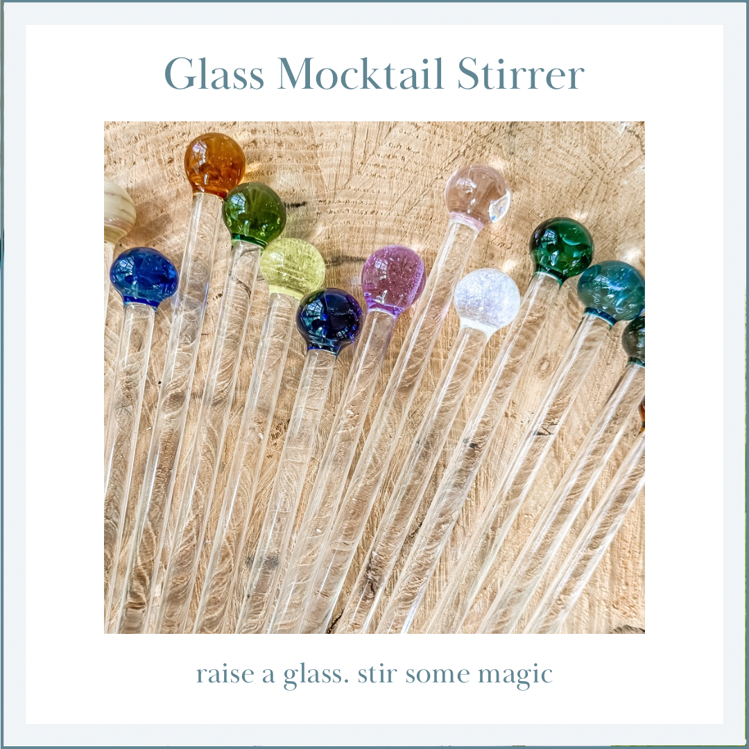 Flat lay of individual glass mocktail stirrers with colorful tops on a wooden surface.