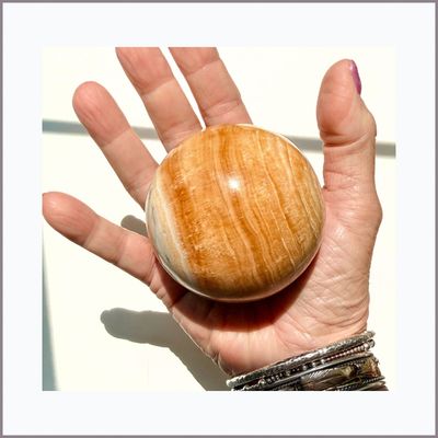 Large banded Orange Calcite sphere in hand
