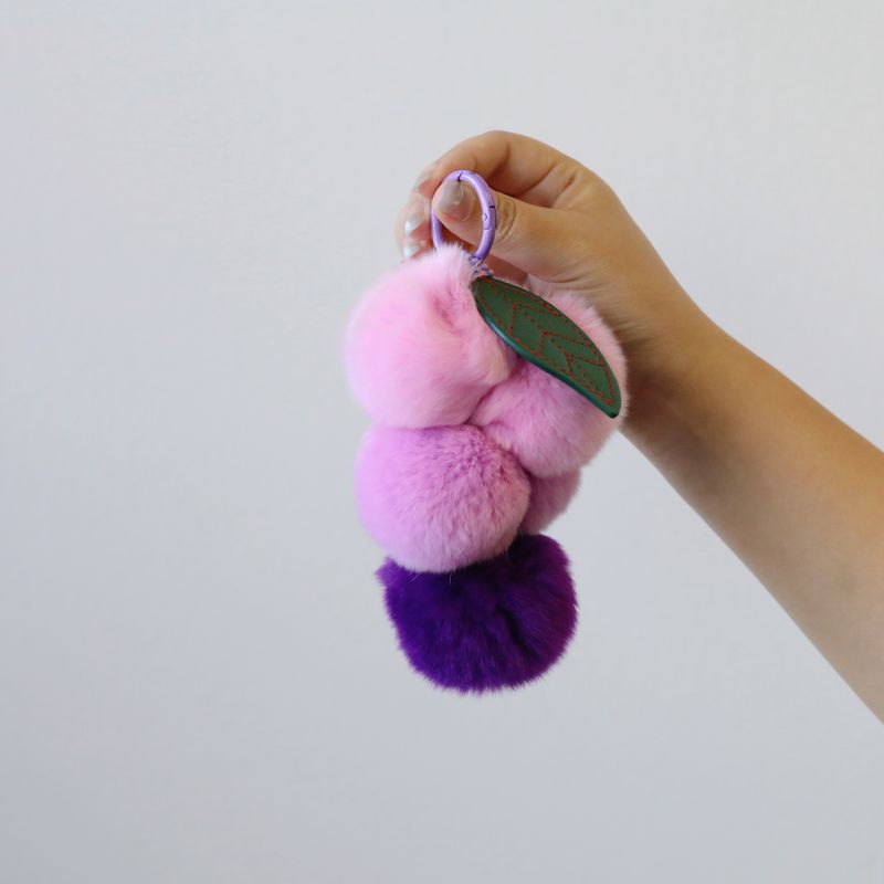 Fluffy grape pom pom keychain held for size reference