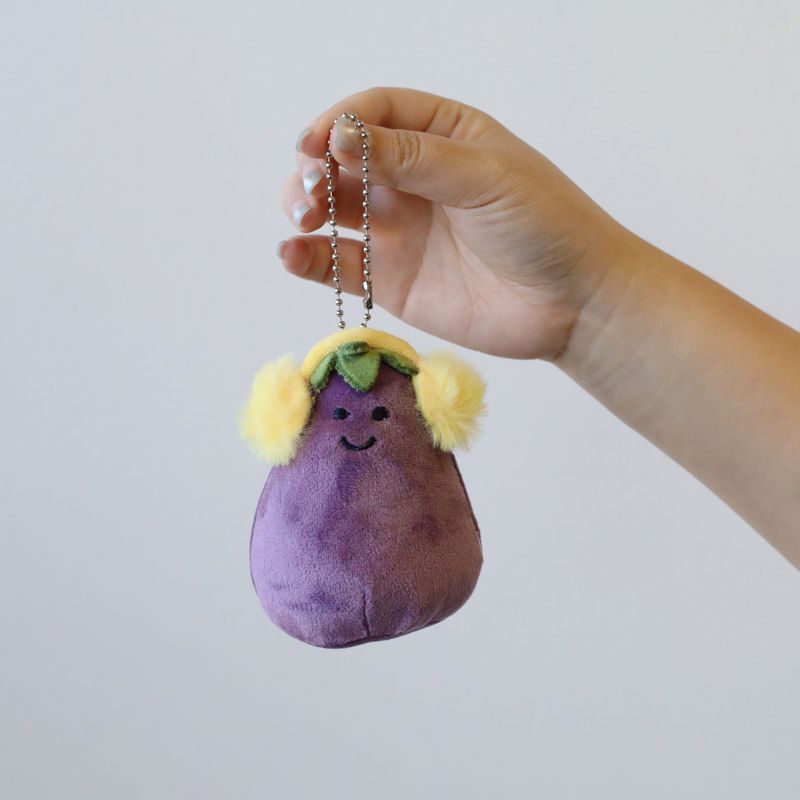 Smiling purple eggplant plush keychain with yellow fluffy earmuffs