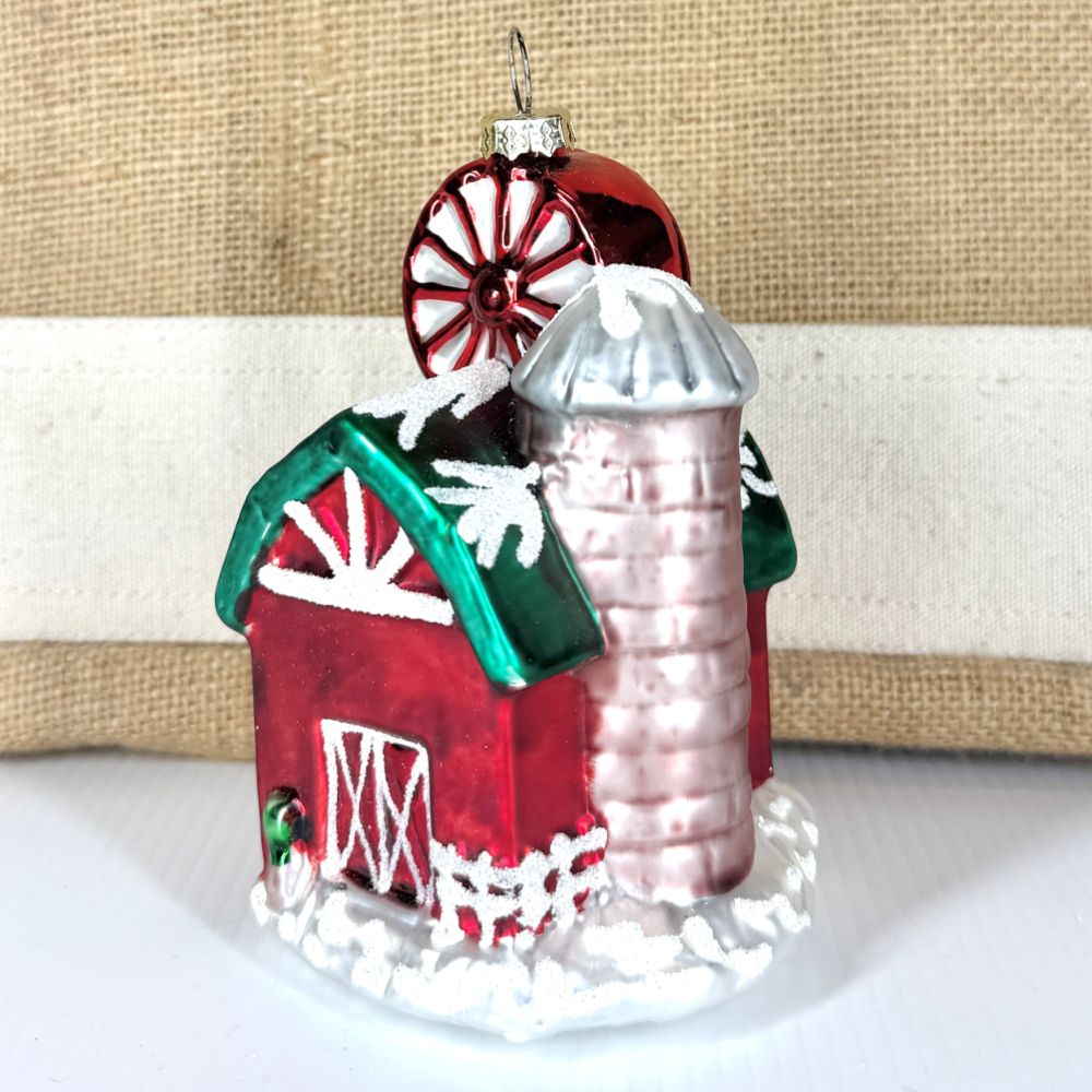 Side view of a glass barn ornament highlighting the tall silver silo and frosted white picket fence detail.