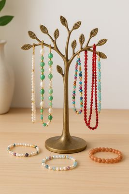 Schmuckständer der einem Baum nachempfunden ist, daran hängen Ketten aus bunten Perlen. Vor dem Ständer liegen eine Armbänder