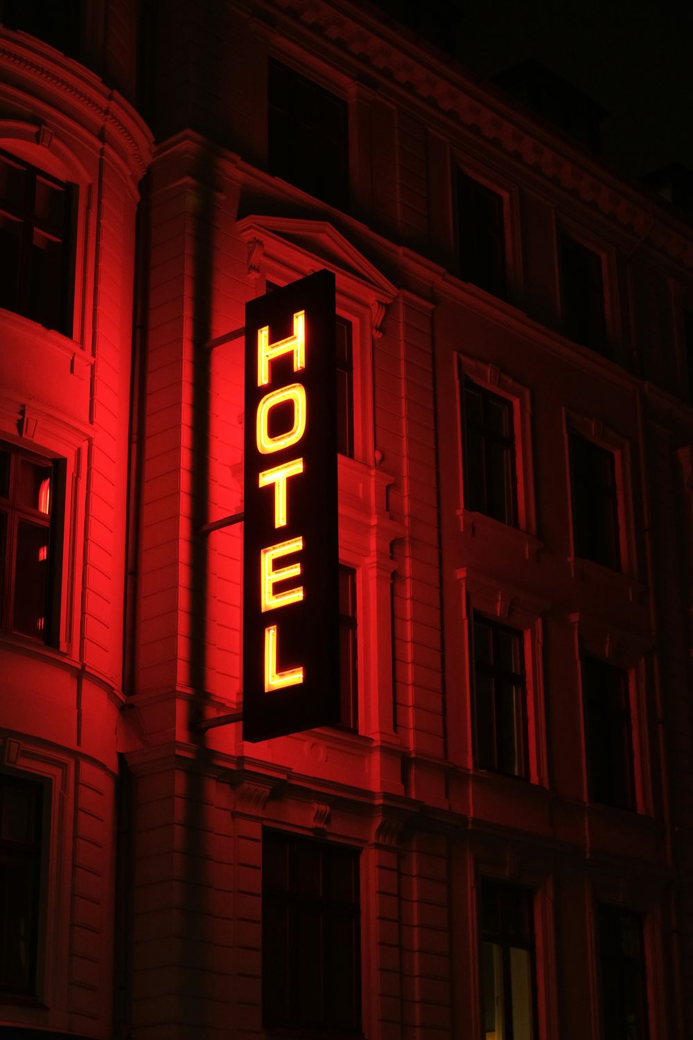 The word hotel written vertically in backlit yellow letters midst red ambient light projected on the building