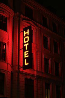 The word hotel written vertically in backlit yellow letters midst red ambient light projected on the building