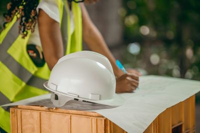 Female member of standbuildteam studying a technical drawing lying with a white construction helmet on a wooden case
