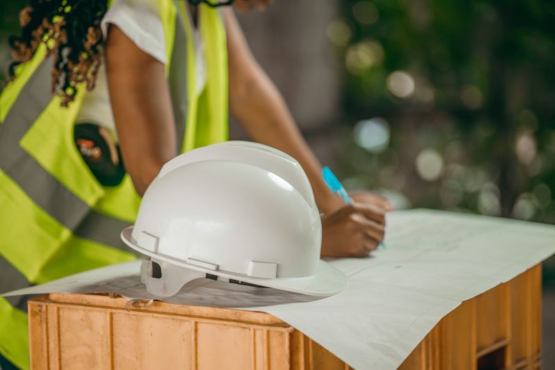 Female member of standbuildteam studying a technical drawing lying with a white construction helmet on a wooden case