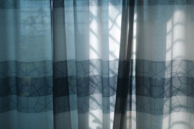 Blueish curtain with sunlight shining on it, but also shades