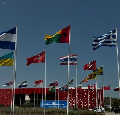 Ship in the water with the city of Athens in the background, partly covered by the Greek flag
