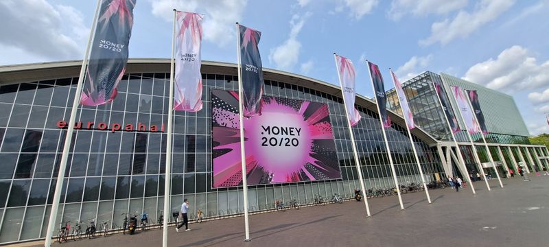 Large Money 20/20 banner on RAI Amsterdam building with branded flags in front.