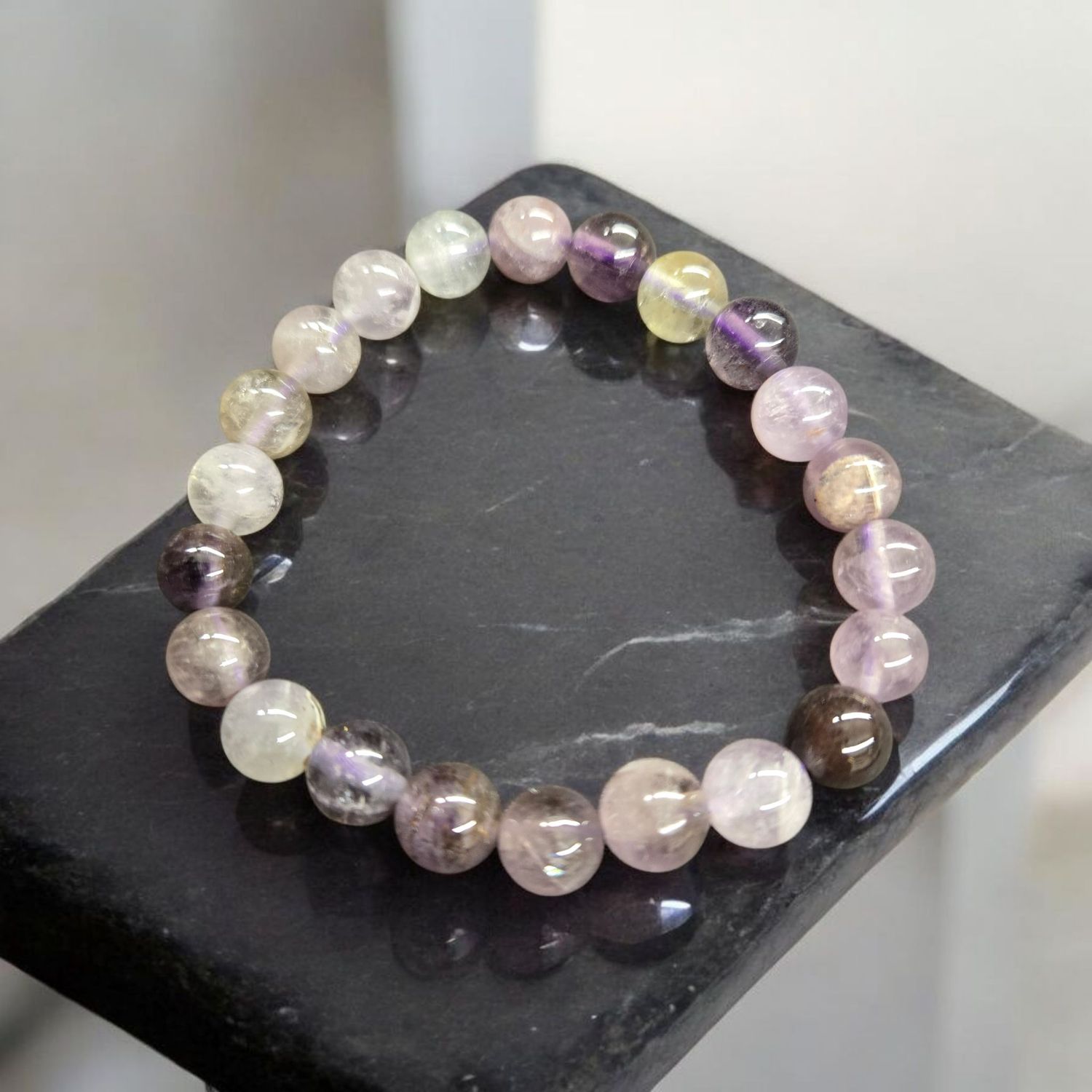 AURALITE 23 8MM BRACELET Auralite 23 8mm round bead stretch bracelet with purple and neutral tones displayed on black stone.
