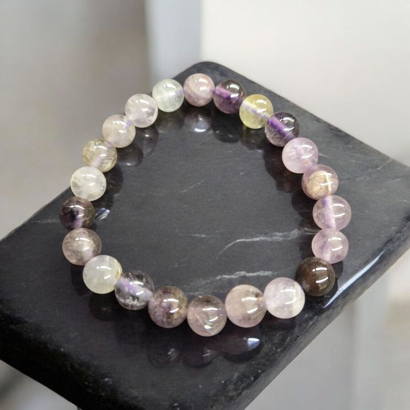Auralite 23 8mm round bead stretch bracelet with purple and neutral tones displayed on black stone.