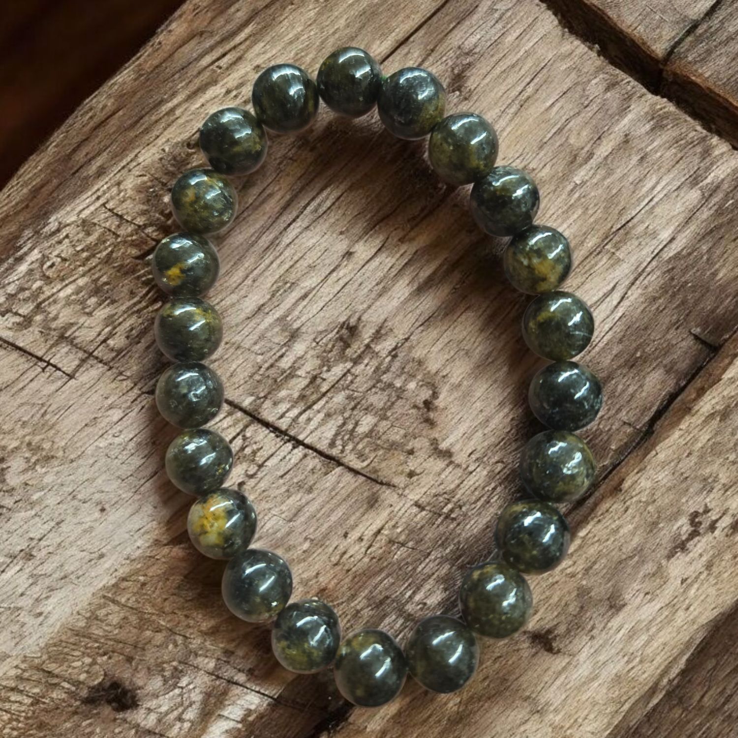 EPIDOTE 8MM BRACELET Epidote 8mm stretch bracelet with deep green and gold tones displayed on rustic wood surface.