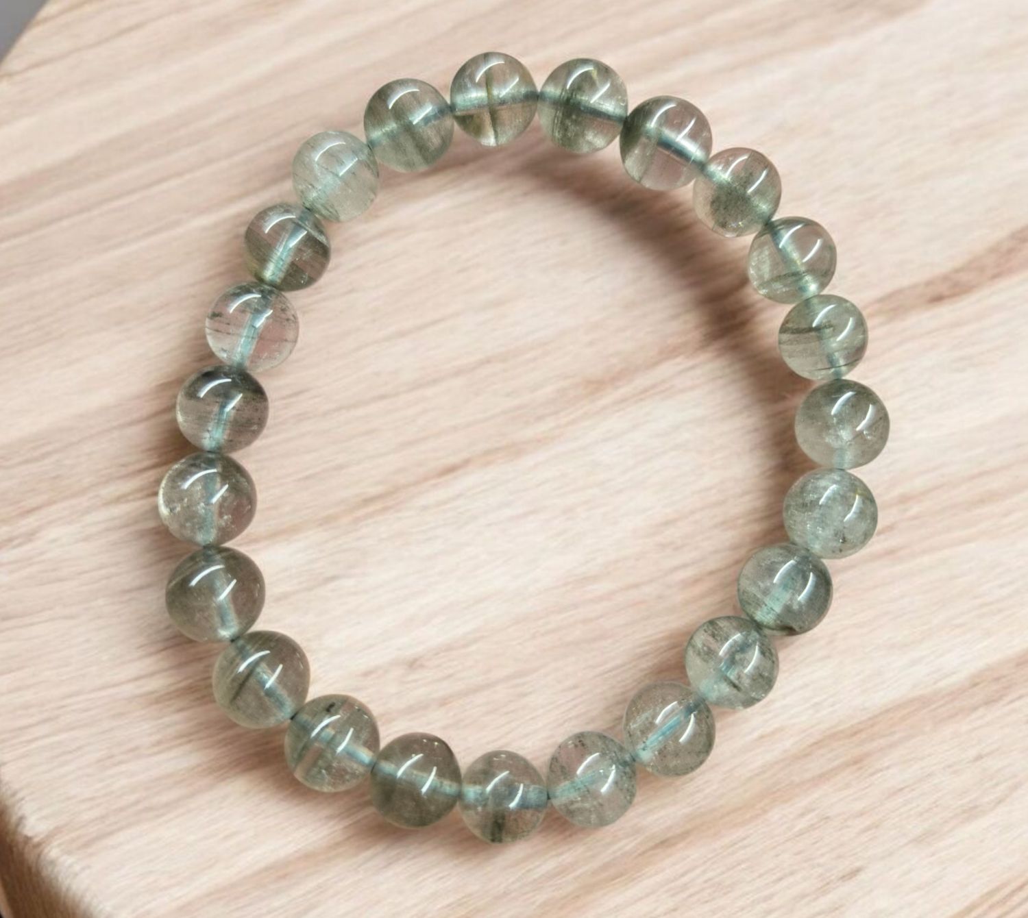 AA LODALITE 8MM BRACELET AA quality Lodalite 8mm stretch bracelet with clear quartz and natural mineral inclusions on a light wood surface.