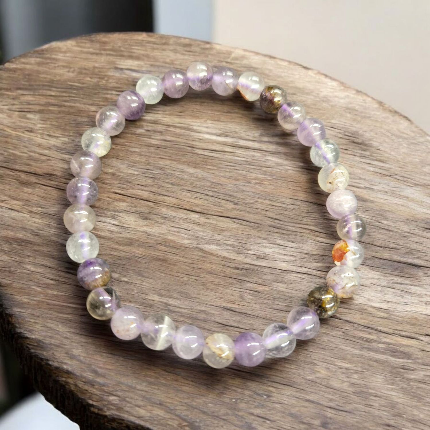 AURALITE 23 6MM BRACELET Auralite 23 6mm bead stretch bracelet with soft lavender and neutral tones displayed on wood surface.