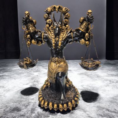 Anubis statue holding golden scales of judgement, kneeling with heart and feather symbols, hand-painted in black and gold.