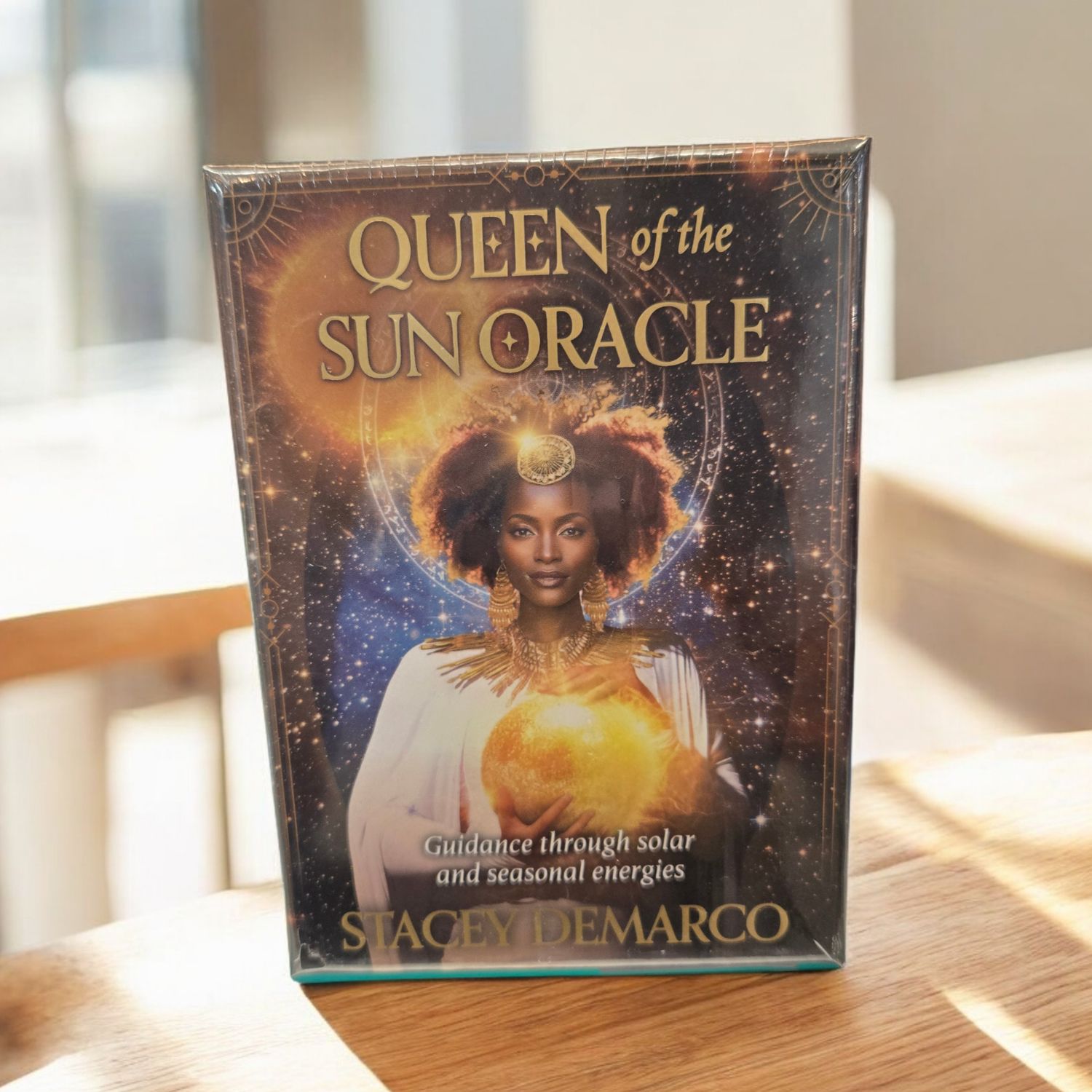 Queen of the Sun Oracle deck front featuring solar goddess holding glowing sun with celestial artwork by Stacey Demarco