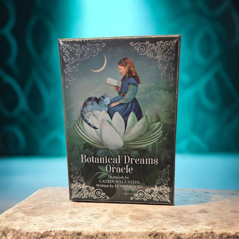 Botanical Dreams Oracle deck front showing girl reading on lotus with cat, crescent moon, and dreamlike botanical artwork