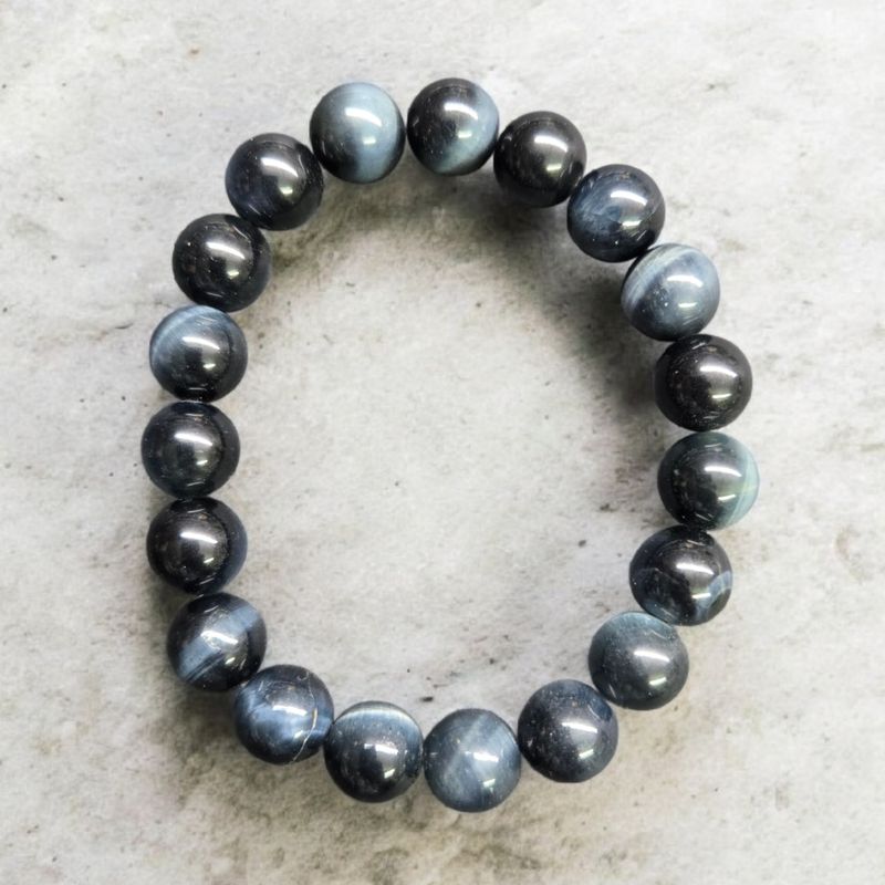 Blue Tiger Eye 10mm stretch crystal bracelet with polished round beads on elastic cord displayed on a light stone background.