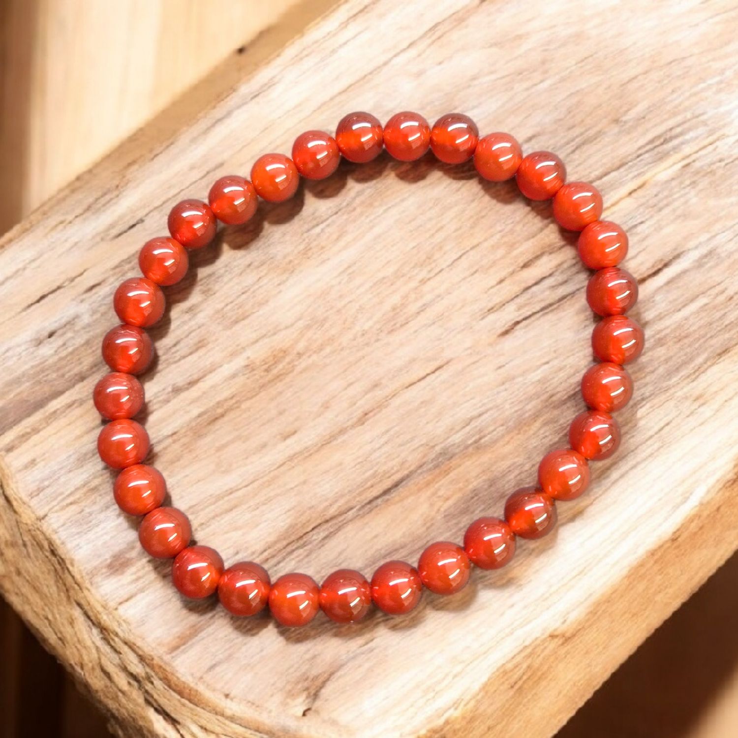 Carnelian 6mm stretch bracelet with polished red-orange round beads displayed on light wooden surface