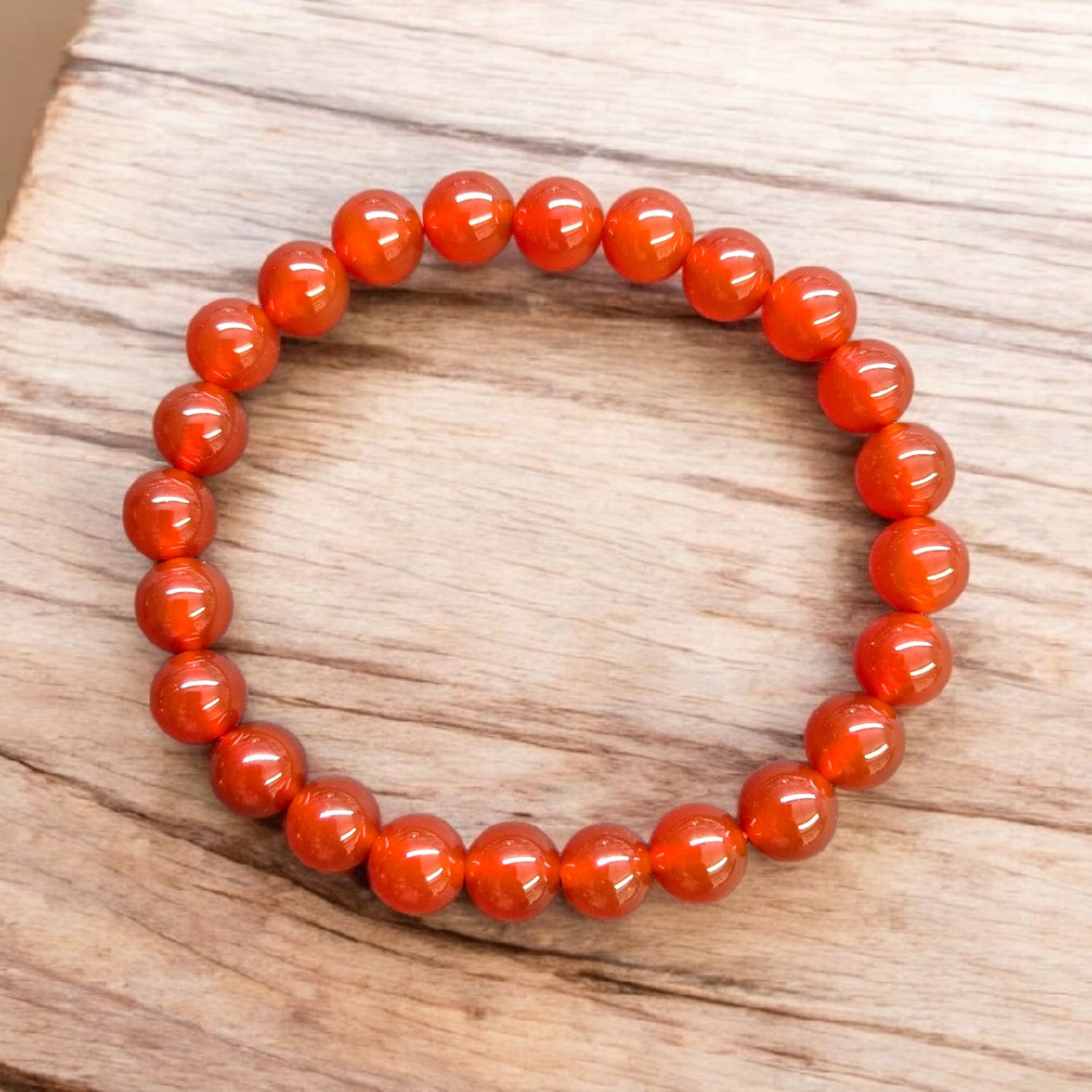 Carnelian 8mm stretch bracelet with polished red-orange round beads displayed on a light wooden surface