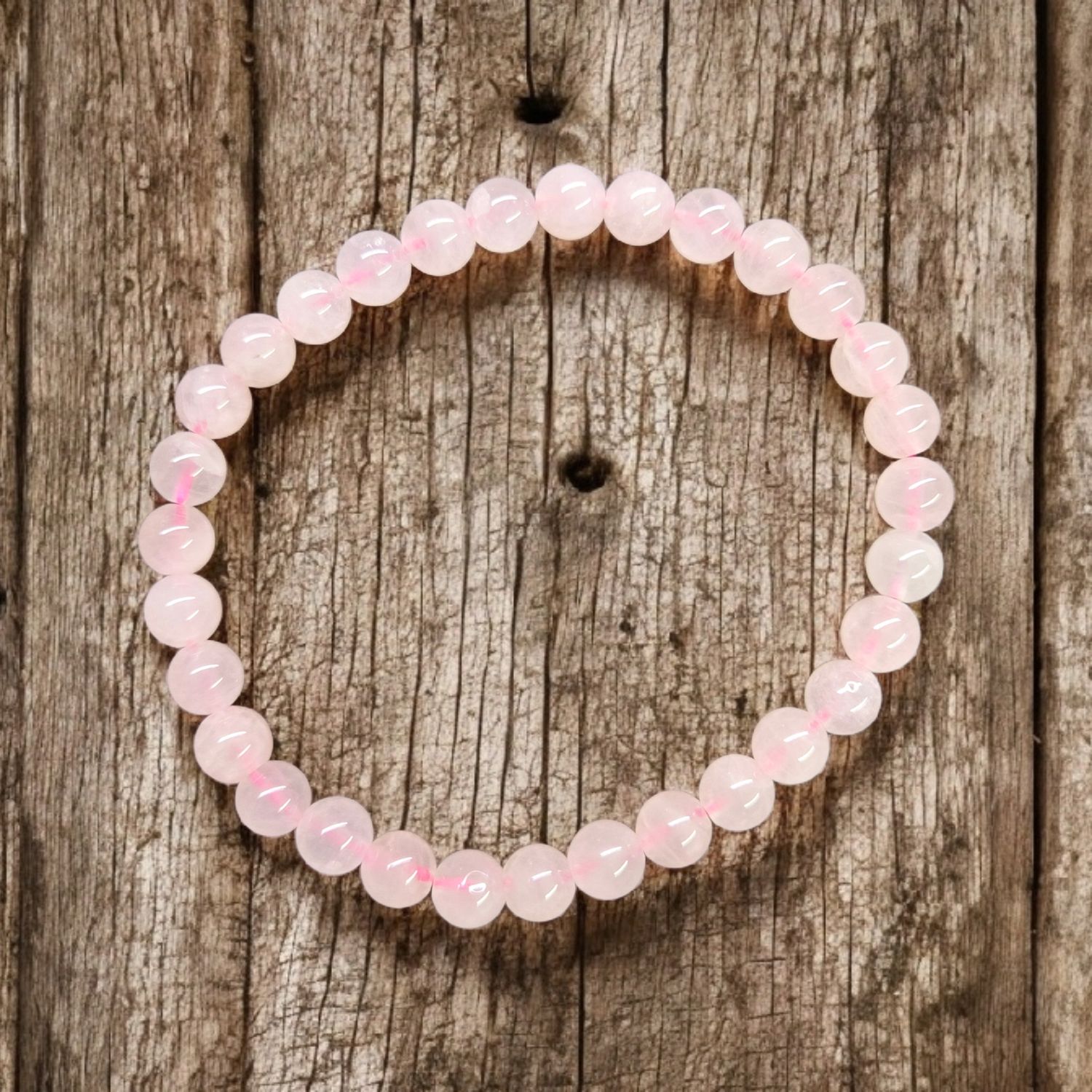 Rose Quartz 6mm stretch bracelet with polished pale pink round beads displayed on rustic wooden background
