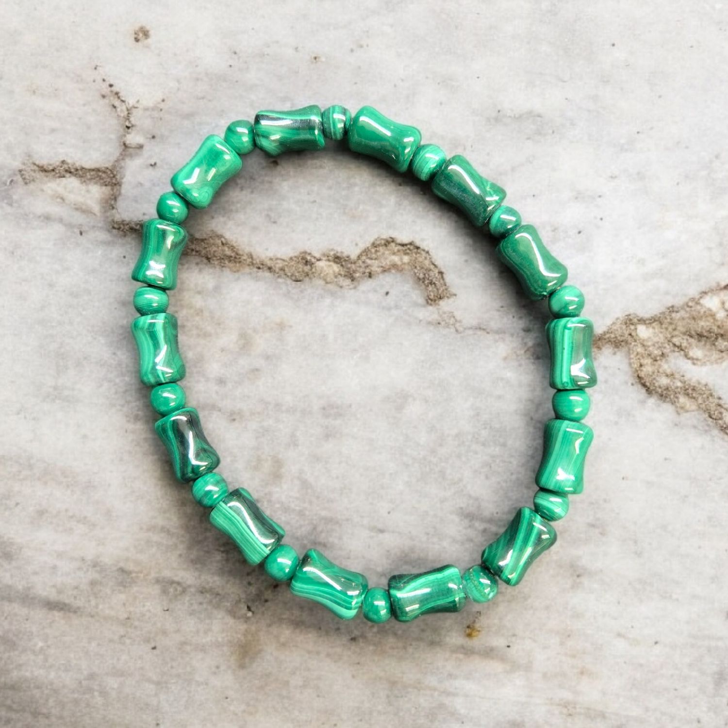 MALACHITE UNIQUE BEADS BRACELET Malachite unique beads stretch bracelet with polished green banded stones displayed on a light marble surface
