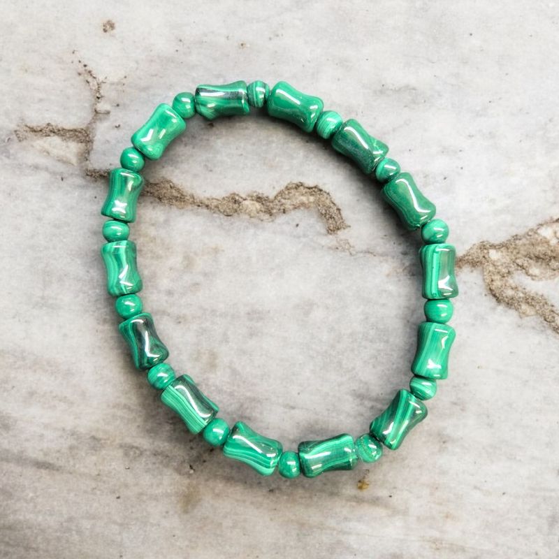 Malachite unique beads stretch bracelet with polished green banded stones displayed on a light marble surface