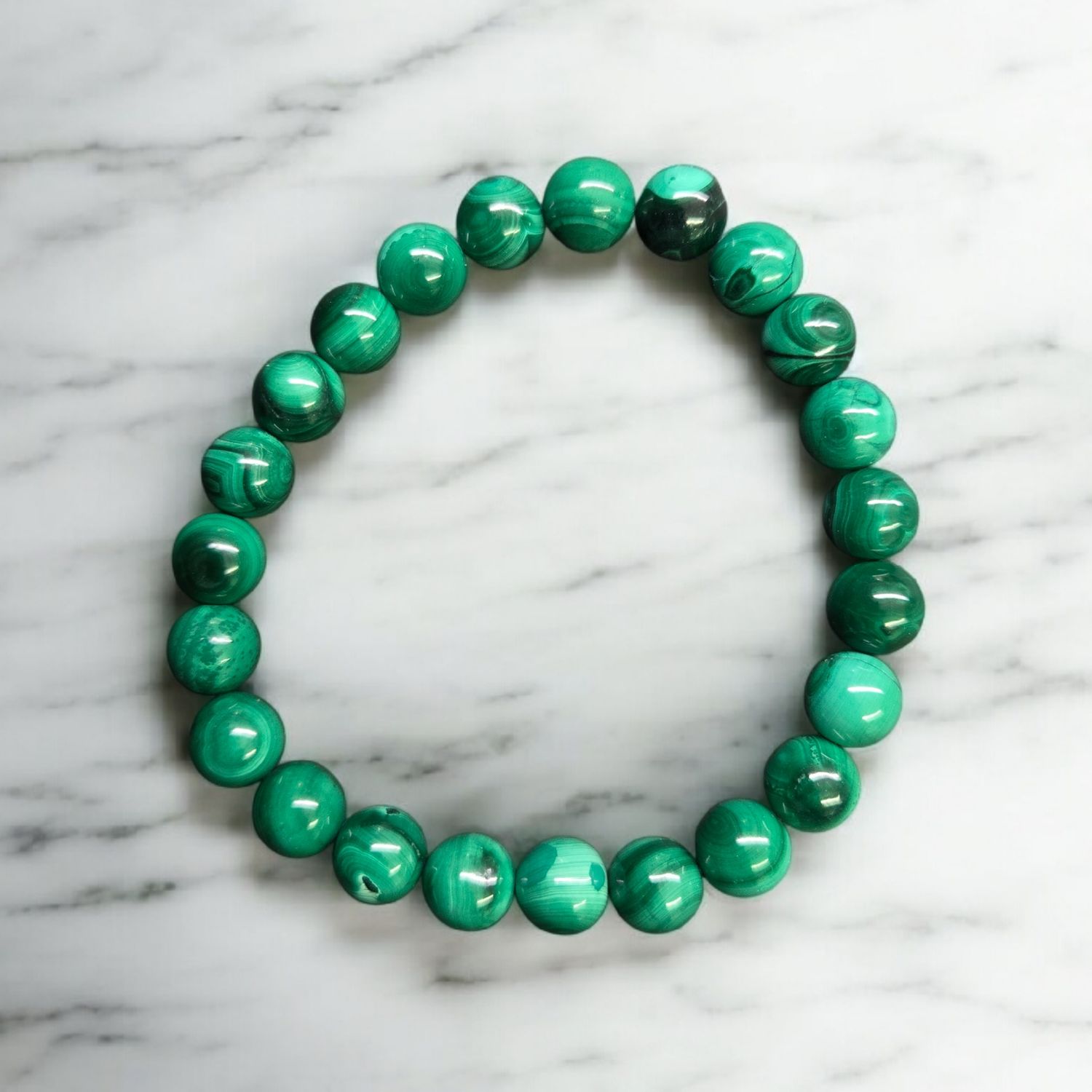 MALACHITE 8MM BRACELET Malachite 8mm stretch bracelet with polished green banded round beads displayed on a white marble surface
