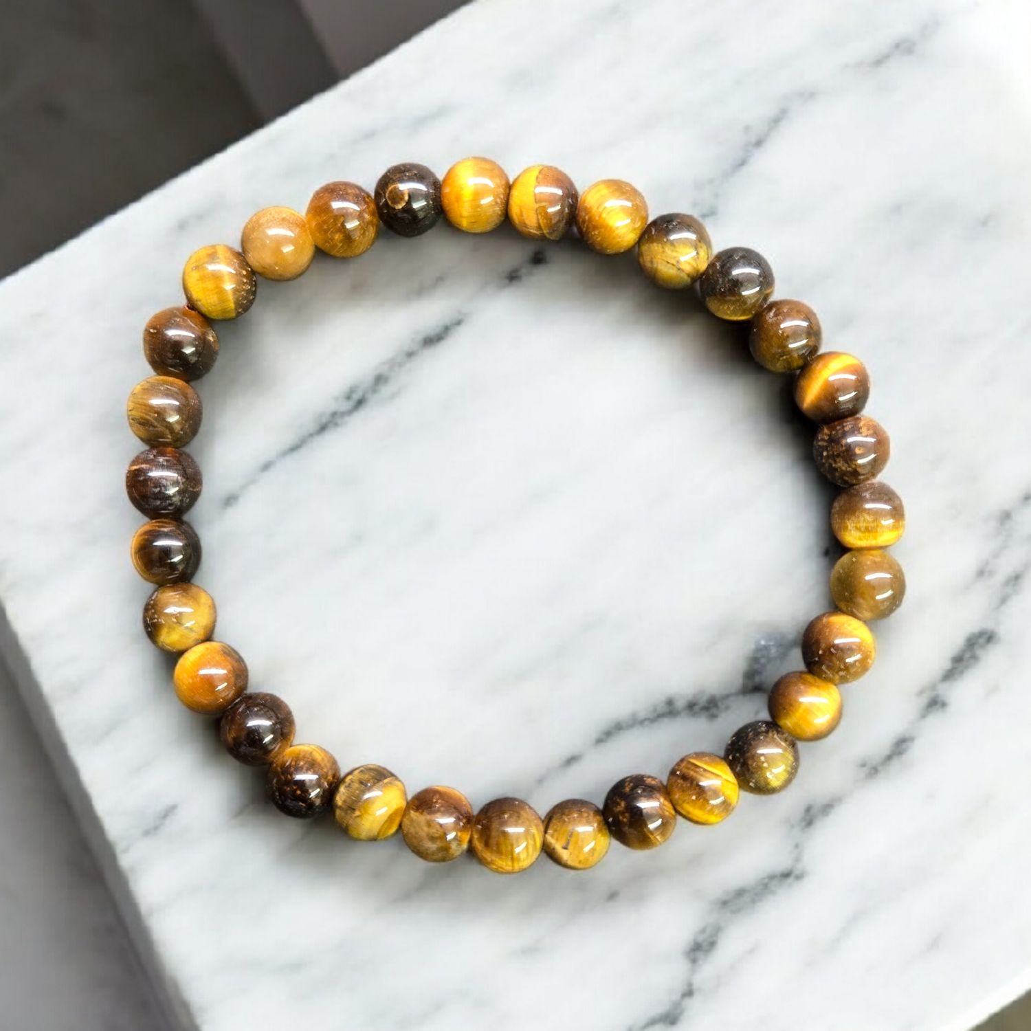 Tiger Eye 6mm stretch bracelet with polished golden brown round beads displayed on a white marble surface