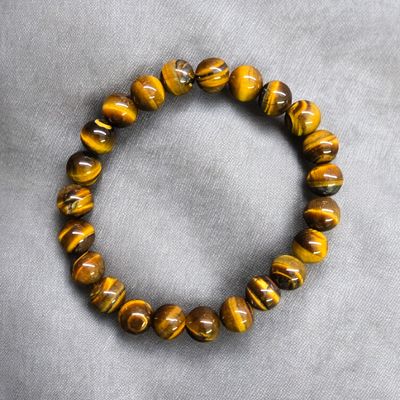Single Tiger Eye 8mm stretch bracelet with polished round golden brown beads on gray fabric
