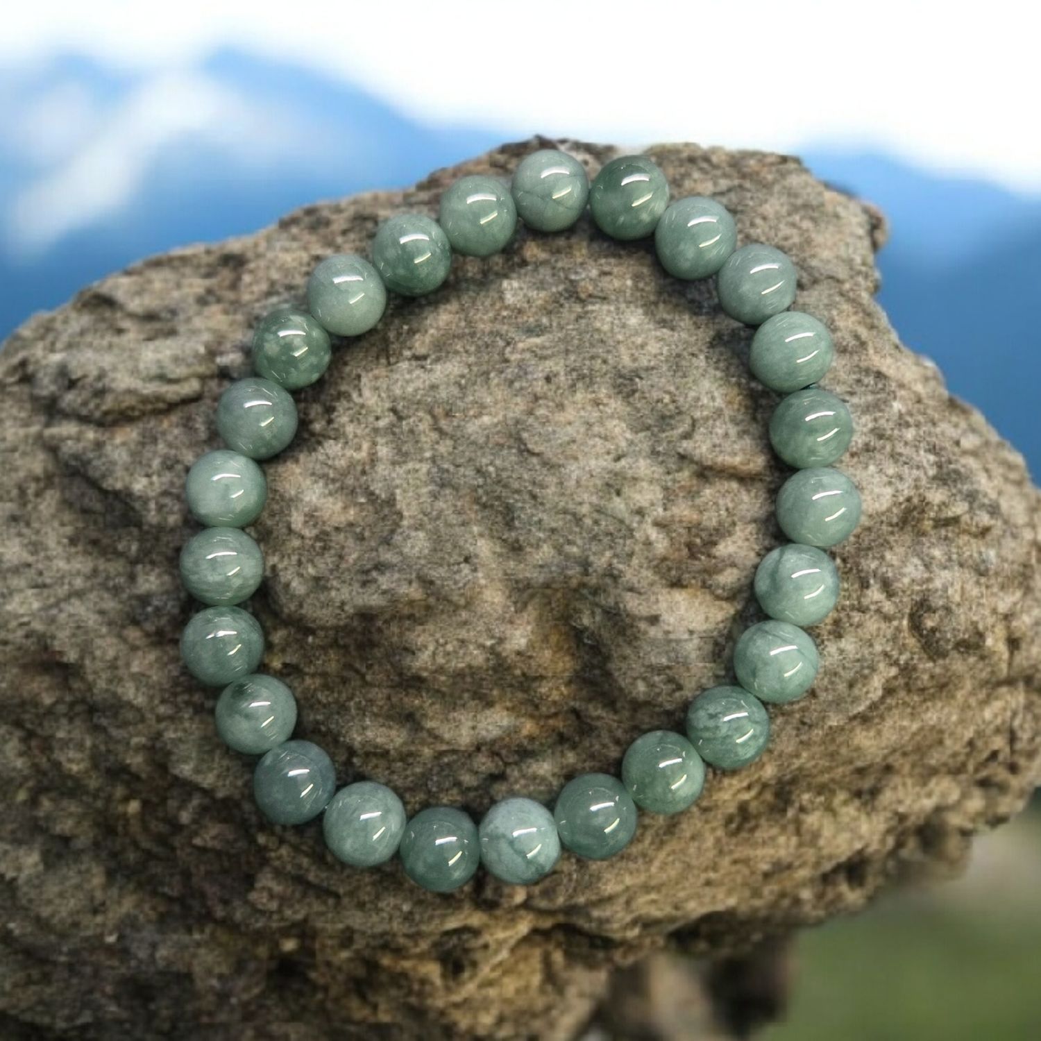 Single jade jadeite 8mm stretch bracelet displayed on stone with soft blue sky background