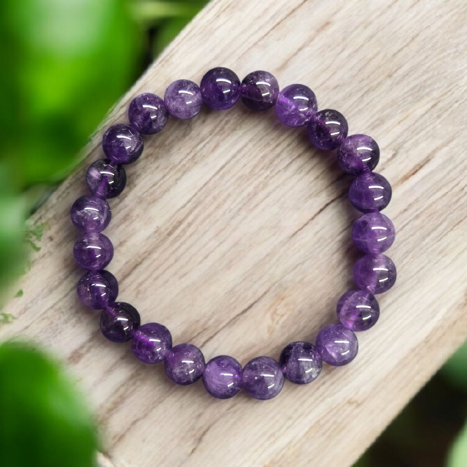 AMETHYST 8MM BRACELET Amethyst 8mm stretch bracelet on wood with greenery, polished purple crystal beads