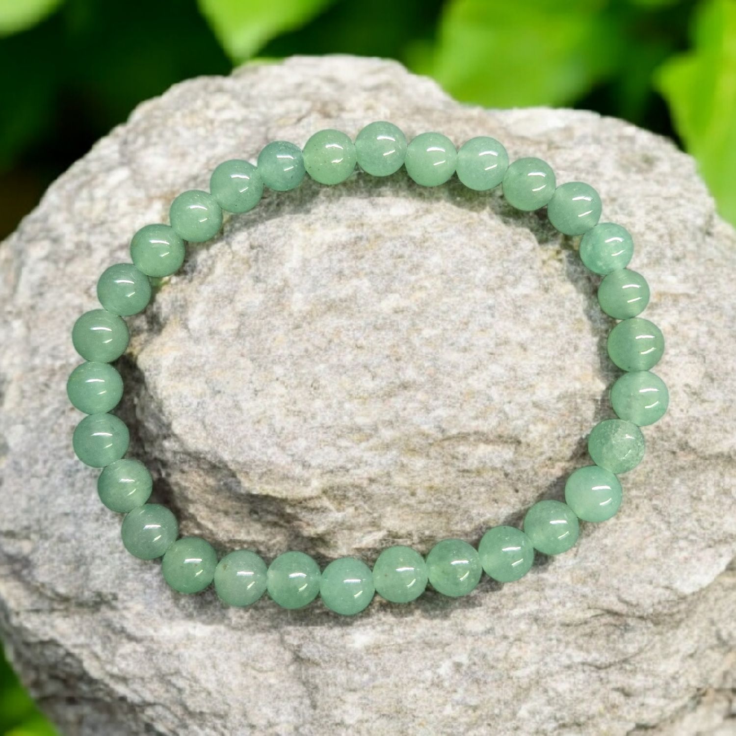 Green Aventurine 6mm stretch bracelet displayed on light stone with green foliage background