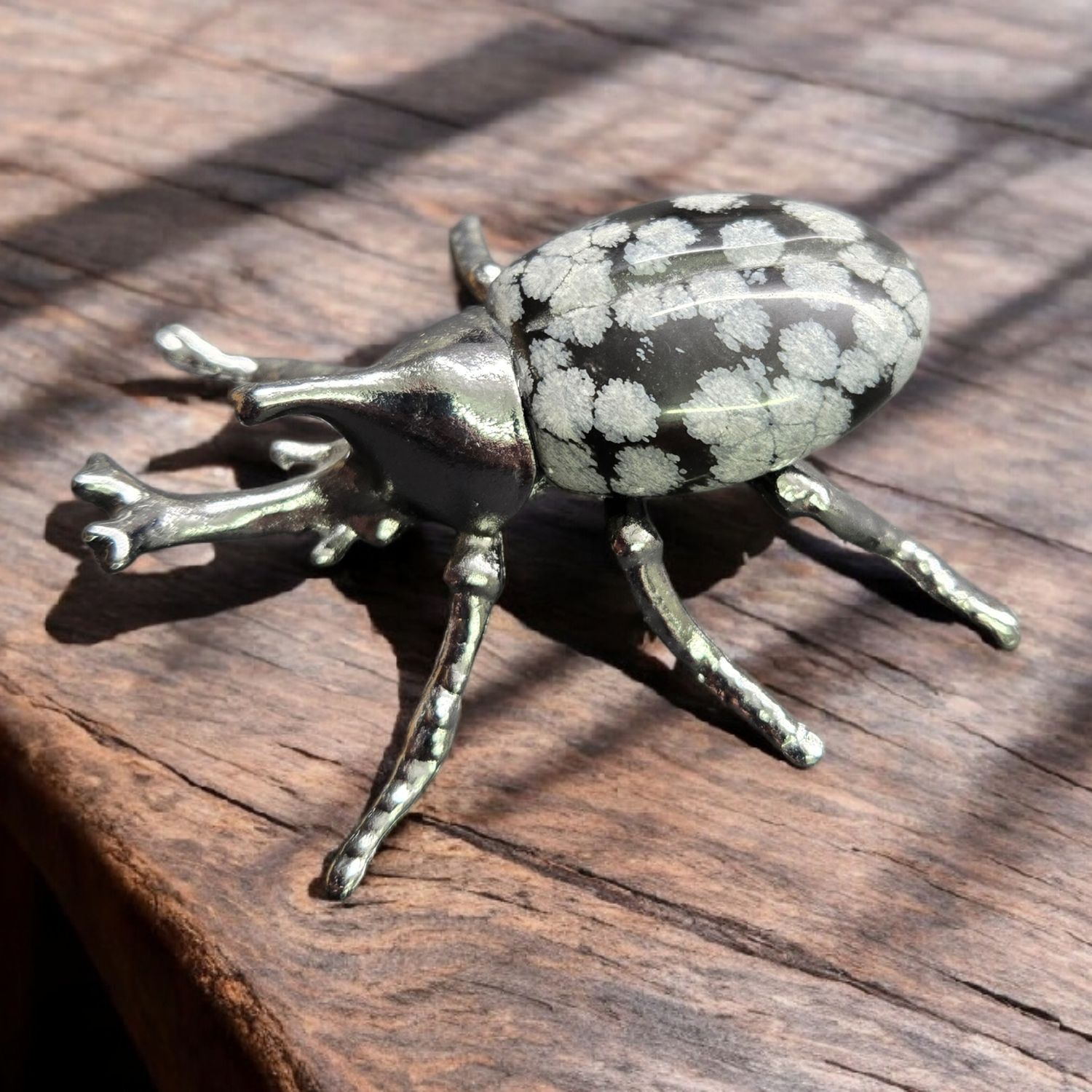 SNOWFLAKE OBSIDIAN BEETLE Snowflake Obsidian beetle carving with metallic legs on wooden surface